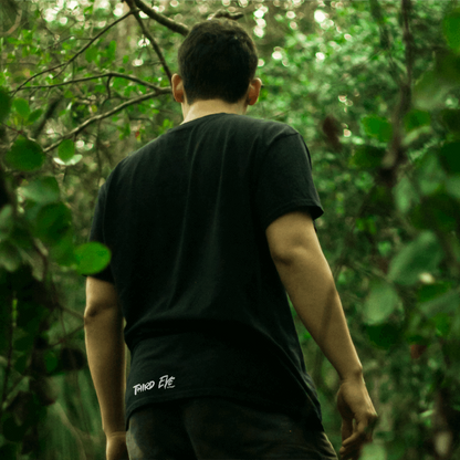 A photo taken from behind. A man walking through the woods wearing a Third Eye Clothingblack tee.